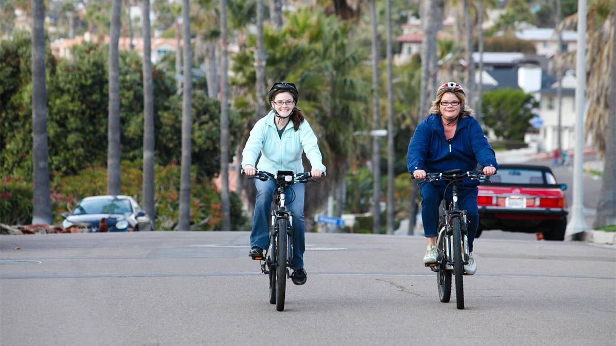 2 Women Riding Bikes Down a palm tree lined Street along La Jolla in San Diego, California, USA